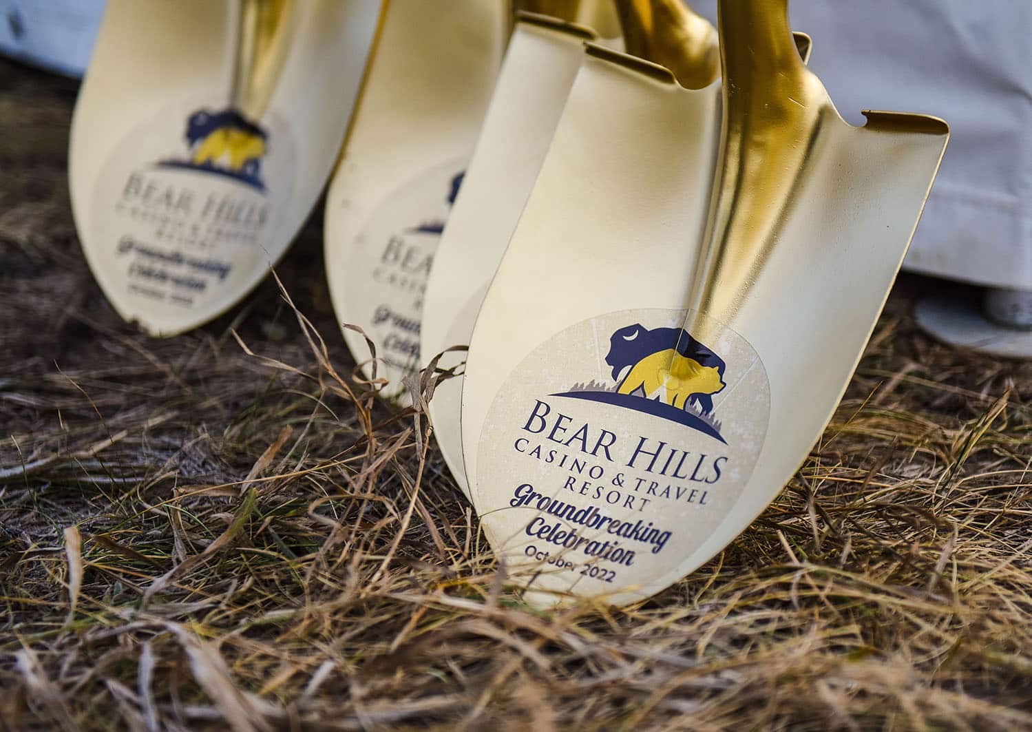 Gold shovels sitting on grass with the Bear Hills logo and text that reads "Groundbreaking Celebration October 2022"