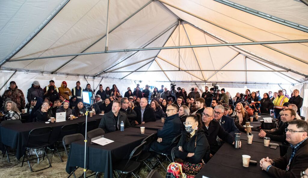 A crowd of about 50 people, some seated at black tables, other in the back are standing